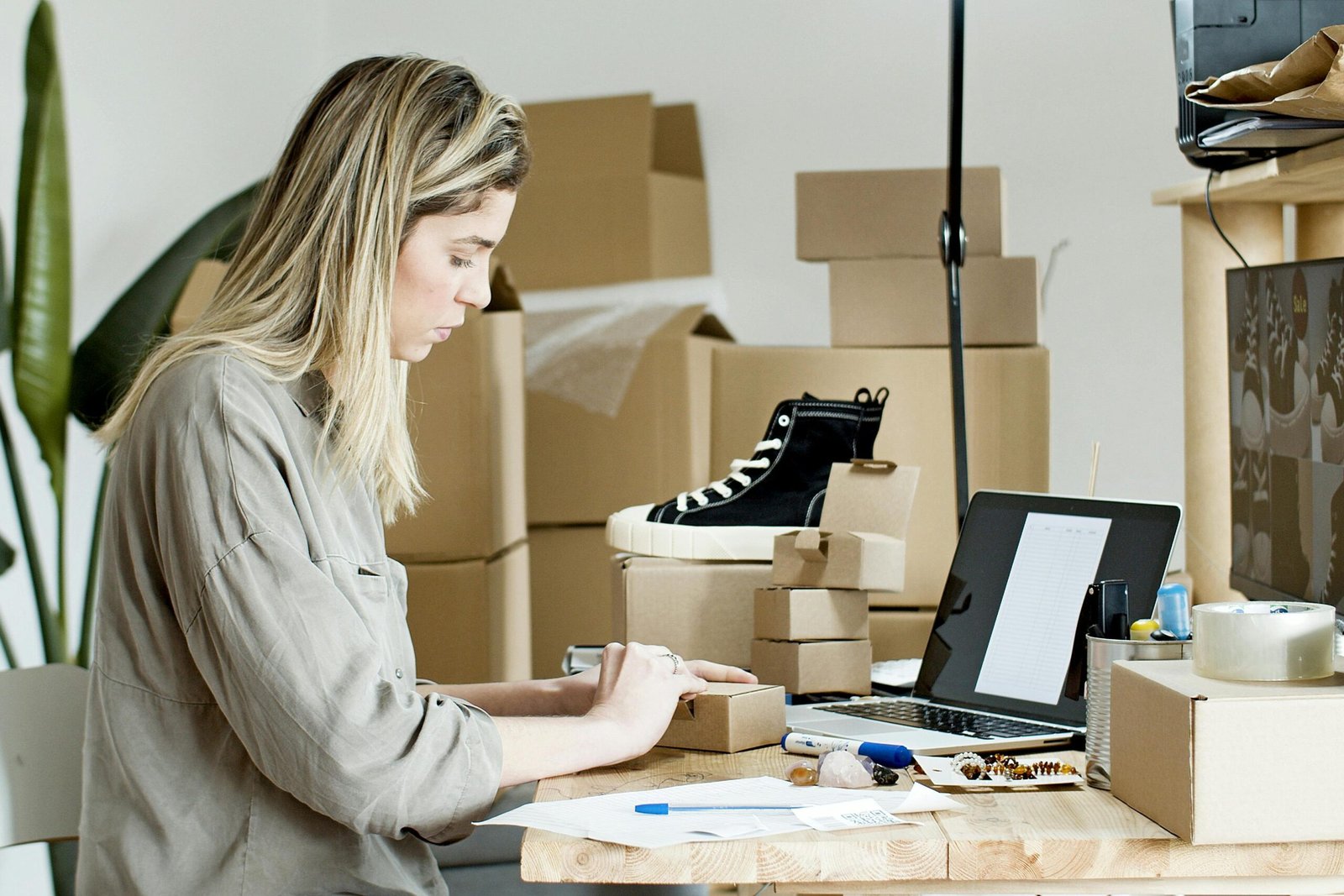 A woman packing boxes for her online store, surrounded by packaging materials and a laptop.